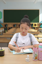 Girl sitting at a desk in a classroom with books and stationery around
